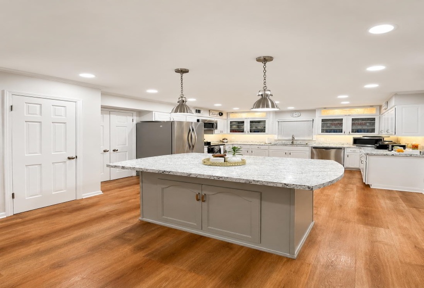 Kitchen featuring a central island with a light-toned countertop, wood-finish flooring, recessed lighting, white cabinetry, and stainless steel appliances