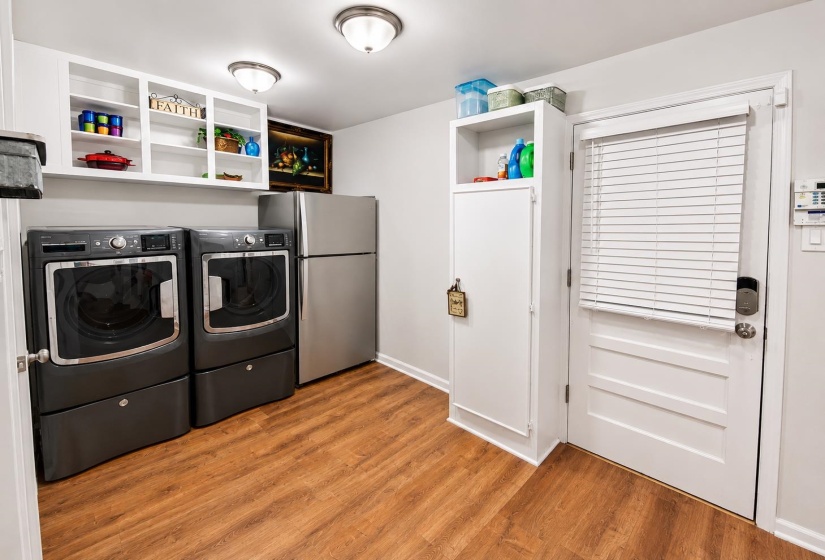 Laundry area featuring wood-finish flooring, white built-in cabinetry, and a paneled exterior door with blinds