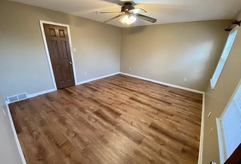 Spacious room featuring wood-finish flooring, neutral-toned walls, white baseboards, and a ceiling fan with integrated lighting