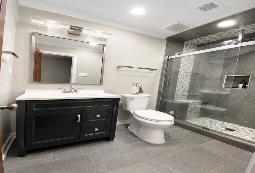 Contemporary bathroom featuring a spacious shower with a sliding glass door, mosaic pebble floor, built-in bench, and recessed shelf