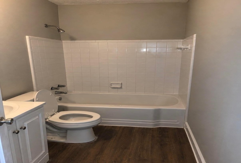 Bathroom featuring a white subway tile tub surround, white bathtub, wood-finish flooring, and a white vanity with a countertop sink