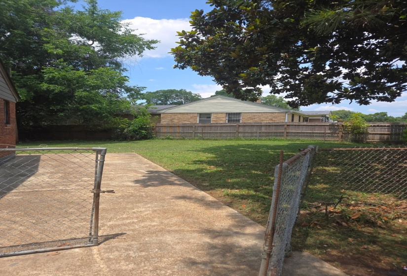 Expansive grassy yard area with a concrete pathway and chain-link fencing