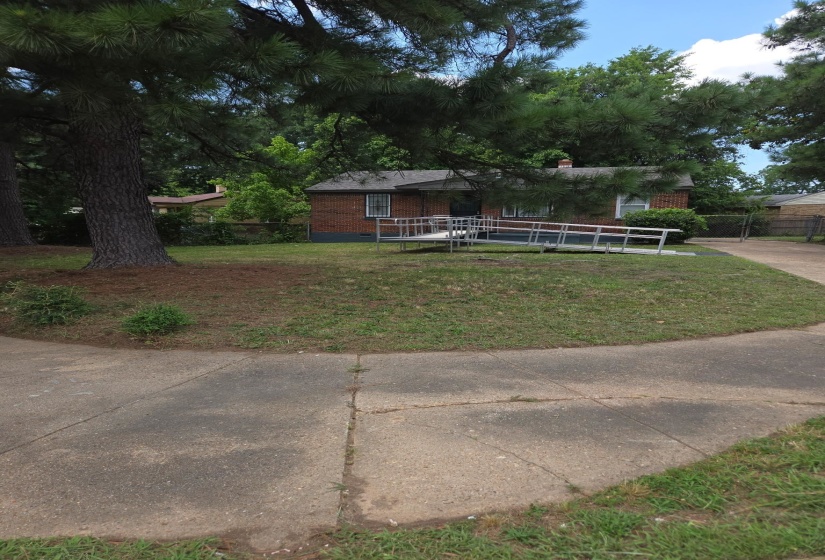Brick facade home featuring a wheelchair ramp entry, mature trees, and a sloped front lawn