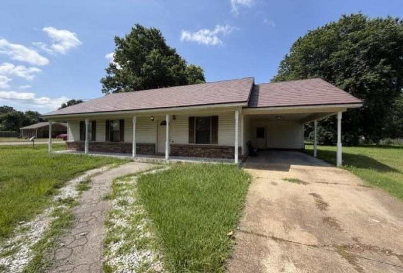 Ranch-style residence featuring a covered front porch with white columns, a stone veneer foundation, and a brown shingle roof