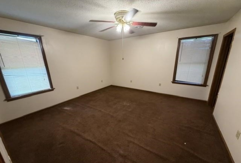 Spacious room featuring neutral painted walls, brown carpeting, and two windows with blinds