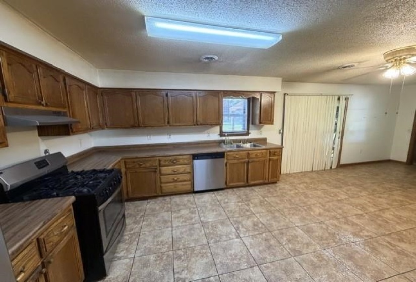 Kitchen featuring wood cabinetry, stainless steel range, stainless steel dishwasher, double basin sink, and tile flooring