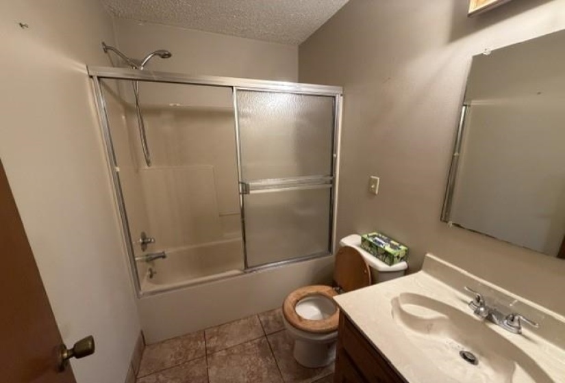 Bathroom featuring a built-in tub with a sliding glass enclosure, tile flooring, a single vanity with an integrated sink, and a wall-mounted mirror