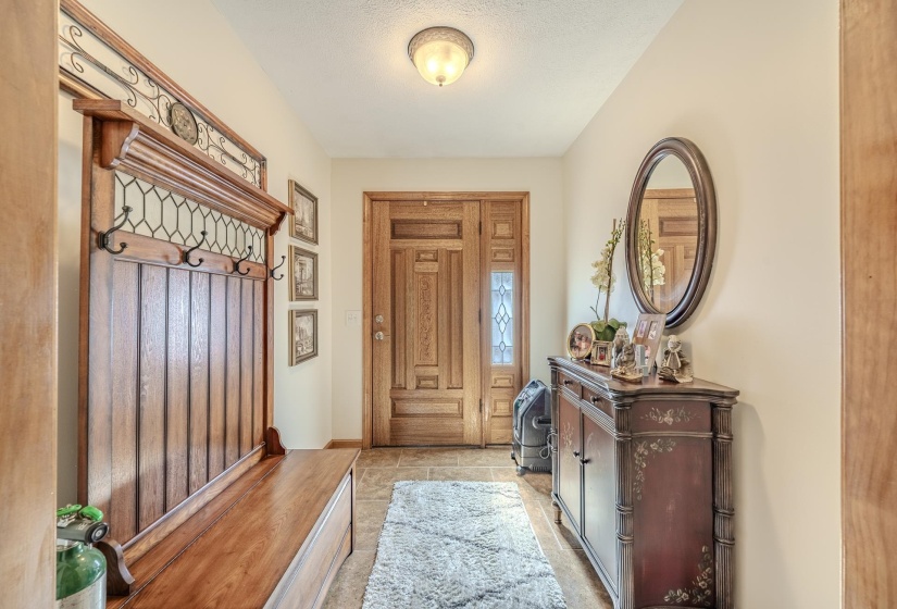 Entryway featuring a wood-panel accent wall with hooks, tile flooring, and a decorative wooden door with a sidelight
