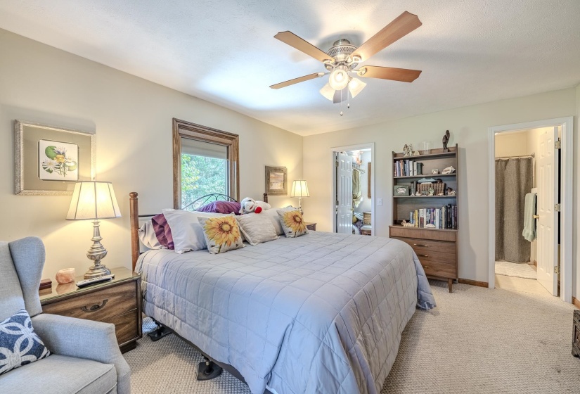 Carpeted bedroom with a ceiling fan, recessed window, and wood-finish nightstands