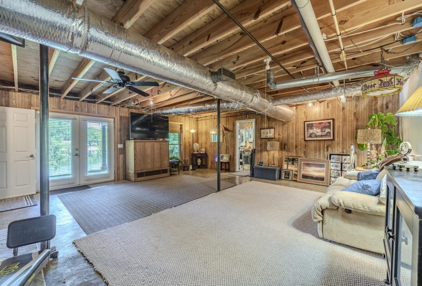 Spacious lower-level area featuring exposed wood ceiling joists and wood-paneled walls