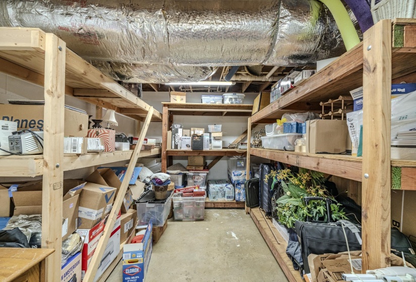Utility space featuring extensive wood shelving, exposed ductwork, concrete flooring, and overhead lighting