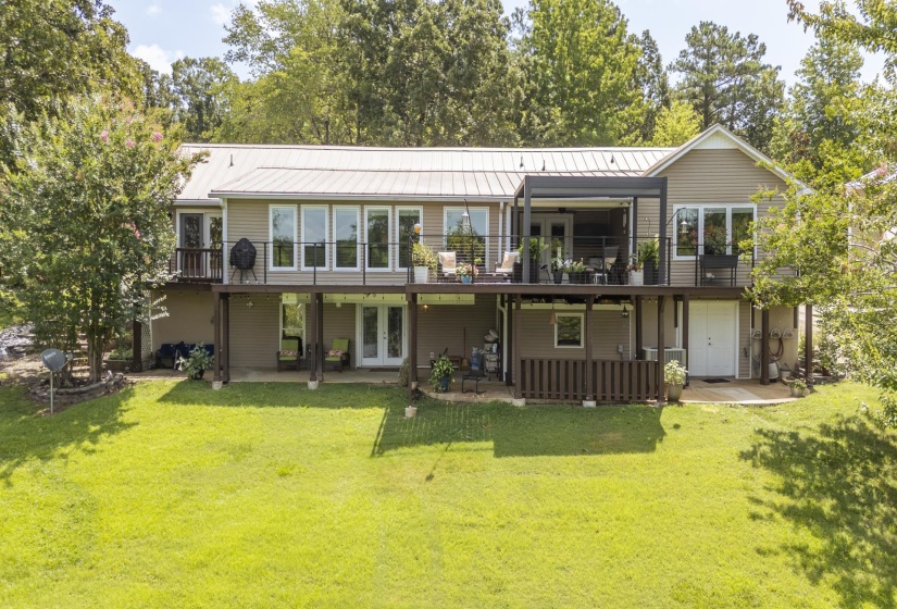 Rear exterior featuring a metal roof, expansive upper deck, lower patio, multiple windows, and a garage door