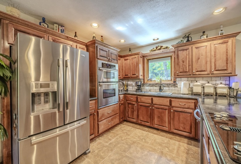 Functional kitchen featuring stainless steel appliances, wood-finish cabinetry, tile flooring, built-in double oven, and a patterned tile backsplash