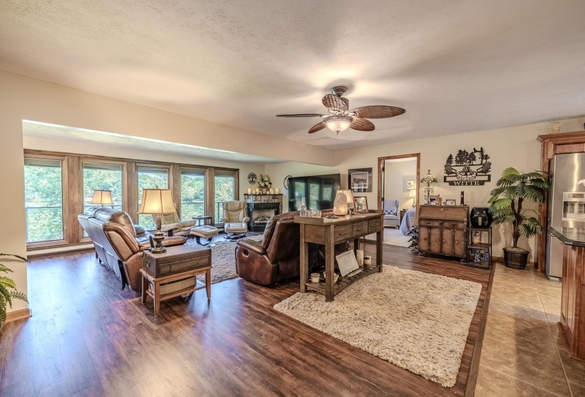 Spacious living area featuring wood-finish flooring, a ceiling fan, and extensive window-framing with a natural backdrop