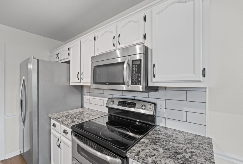 Kitchen featuring white cabinetry, granite-finish countertops, subway tile backsplash, stainless steel appliances, and a built-in microwave