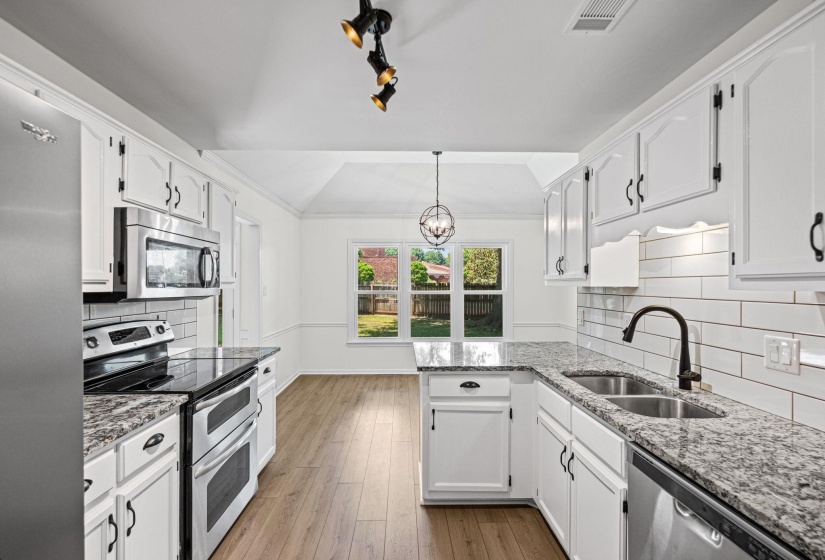 Kitchen featuring white cabinetry with dark hardware, granite countertops, stainless steel appliances, and wood-finish flooring