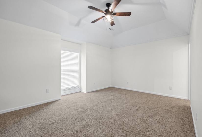 Spacious room featuring vaulted ceilings, light-colored carpeting, and a ceiling fan with integrated lighting