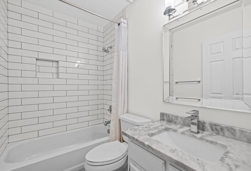 Bathroom featuring a white subway tile shower surround with a recessed niche, a white tub, and a chrome shower head