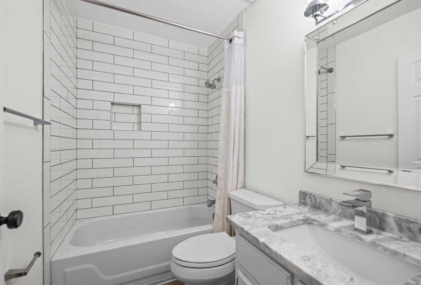 Bathroom featuring a subway tile shower surround with integrated niche, white bathtub, toilet, and vanity with a stone countertop and rectangular sink