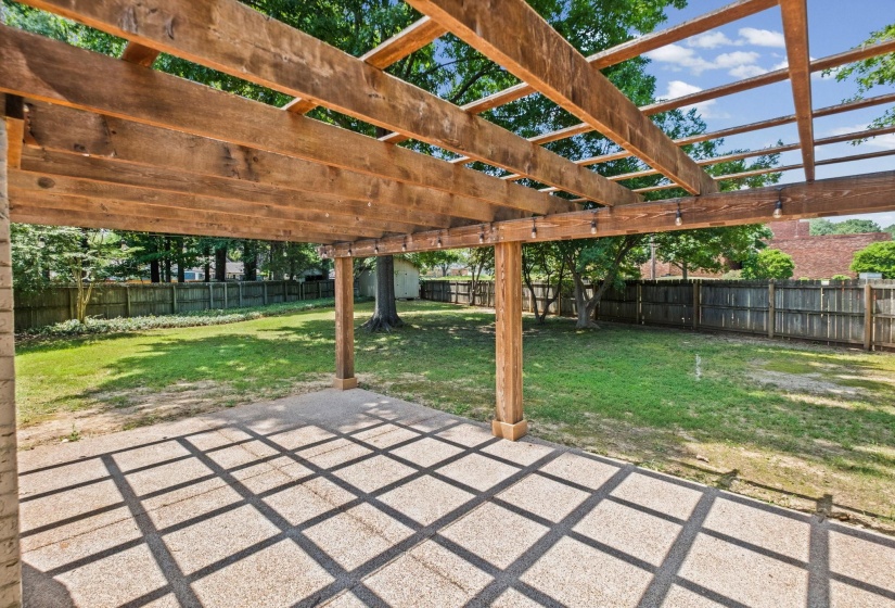 Expansive outdoor patio featuring a wooden pergola with integrated string lighting