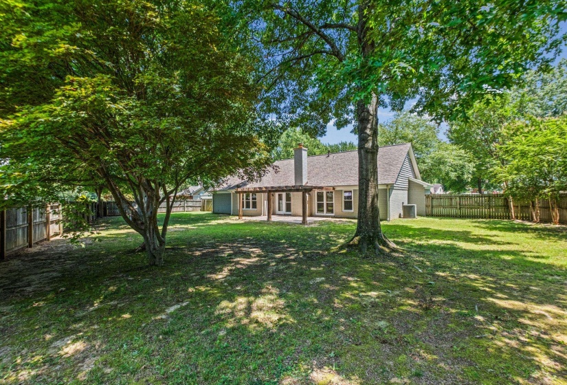 Spacious backyard featuring a pergola-covered patio, mature trees, and a wood privacy fence