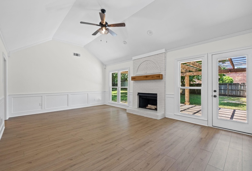 Spacious living area featuring a vaulted ceiling with a ceiling fan, wood-finish flooring, and wainscoting