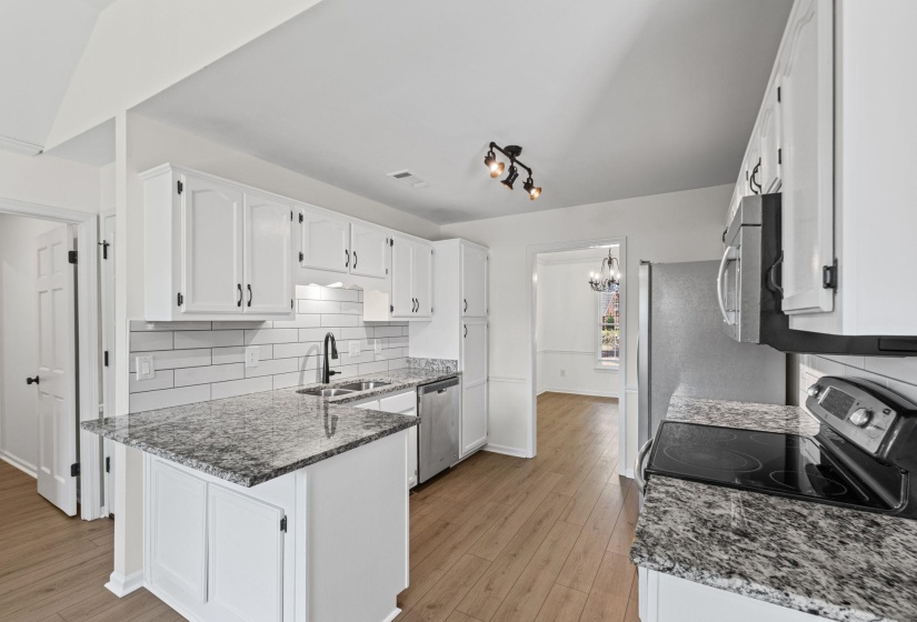 Kitchen featuring white cabinetry, granite countertops, a subway tile backsplash, and wood-finish flooring