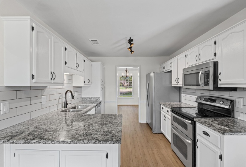 Kitchen featuring white cabinetry with black hardware, granite countertops, white subway tile backsplash, stainless steel appliances, and wood-finish flooring
