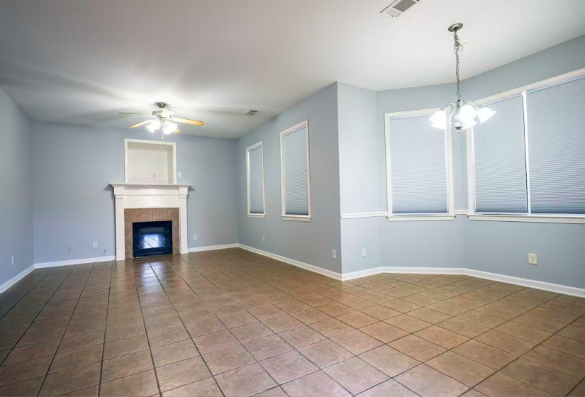 Spacious room featuring tile flooring, a fireplace with a mantel, a ceiling fan, and multiple windows with blinds