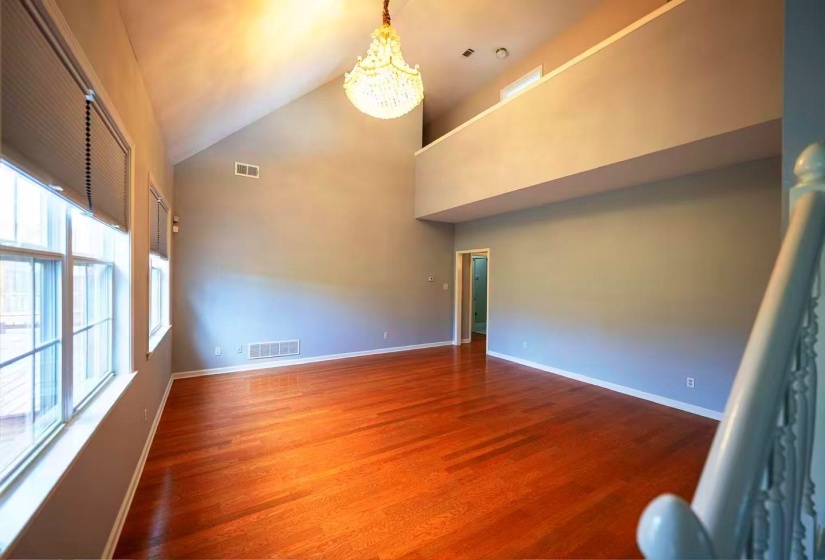 Spacious room featuring soaring vaulted ceilings, a prominent chandelier, rich wood-finish flooring, and multiple large windows
