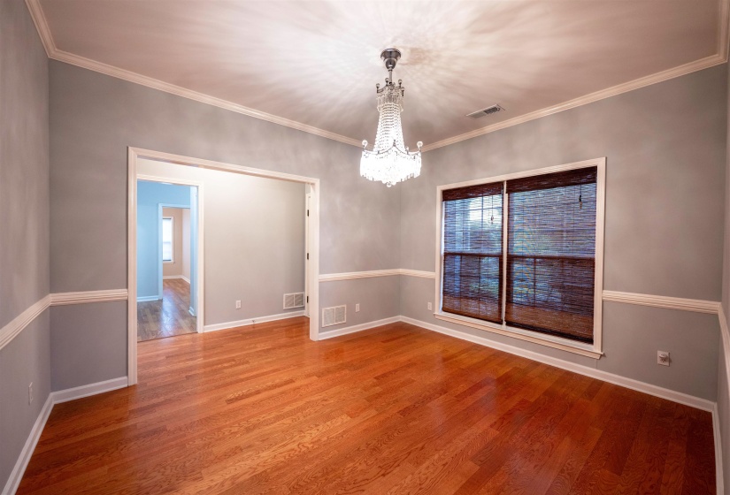 Spacious interior room featuring wood-finish flooring, a decorative chandelier, and a large window with woven blinds