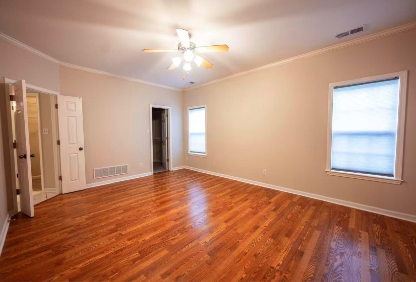Spacious room featuring wood-finish flooring, two windows with blinds, a ceiling fan, crown molding, and two interior doors