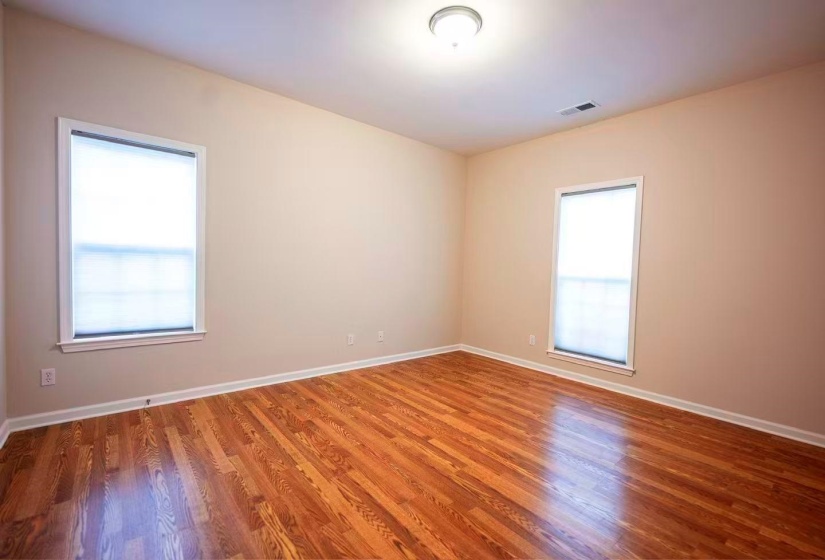 Hardwood flooring throughout, featuring neutral wall paint, white trim, two windows with blinds, and a ceiling-mounted light fixture