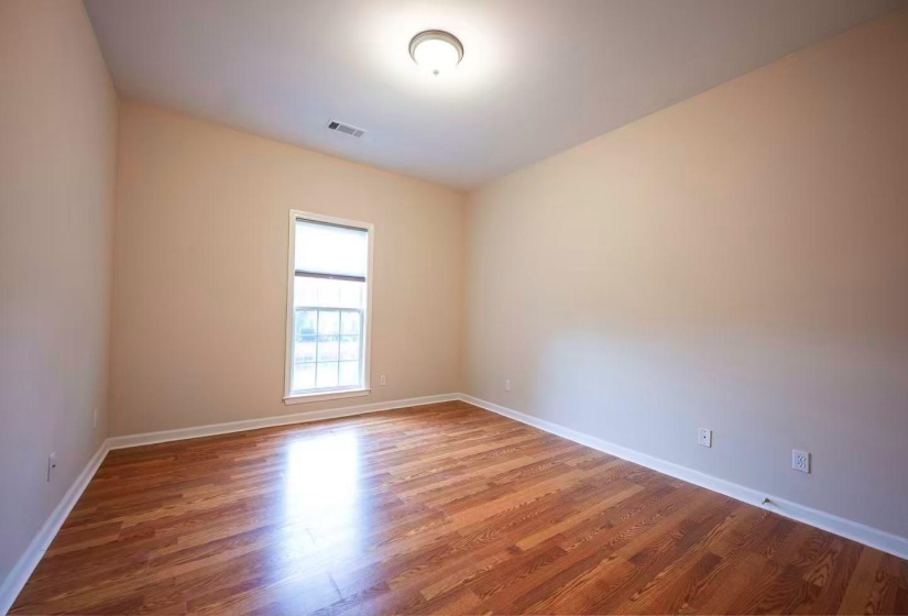 Room featuring wood-finish flooring, neutral wall paint, and a large window with privacy blinds