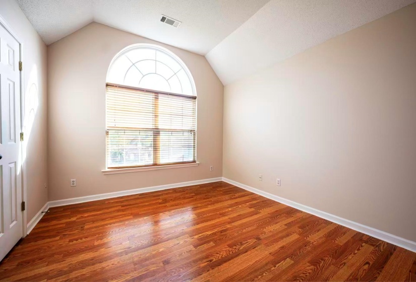 Vaulted ceiling room featuring a large arched window with blinds, wood-finish flooring, and white baseboards