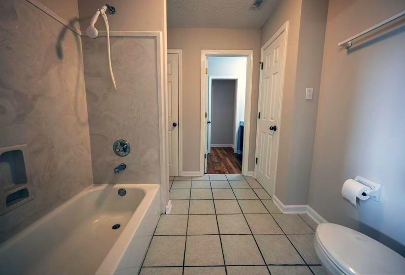 Bathroom featuring a white bathtub with a shower system, tile-finish wall surround, chrome fixtures, and square tile flooring