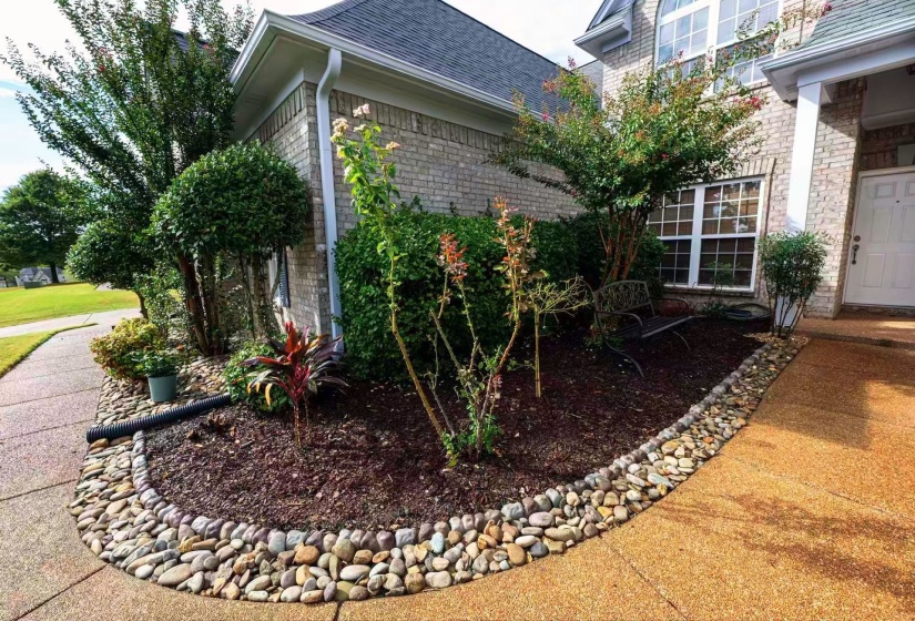 Landscaped garden bed featuring a river rock border, mature shrubs, and young plantings