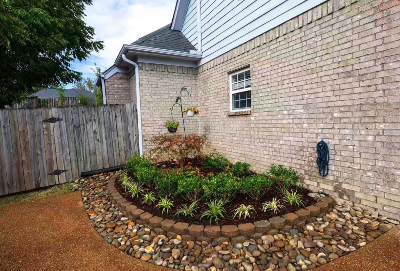 Landscaped garden bed featuring a variety of plants, decorative river rock, and a retaining wall of hexagonal pavers