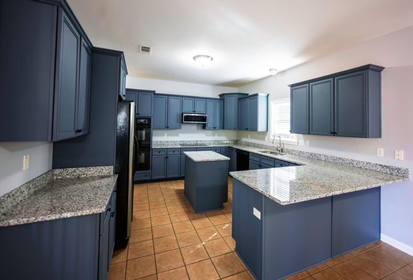 Kitchen featuring abundant navy cabinetry, granite countertops, a central island, built-in double ovens, and tile flooring