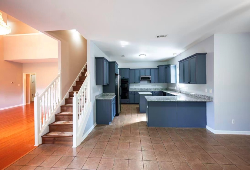 Open-concept living area featuring a kitchen with blue cabinetry and light-toned countertops, tile flooring, and a staircase with white balusters