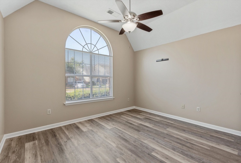 Vaulted ceiling room featuring a large arched window, wood-finish flooring, and a ceiling fan with integrated lighting