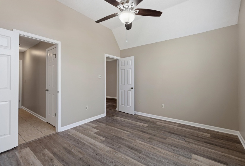 Vaulted ceiling room featuring wood-finish flooring, neutral wall tones, white trim, and a ceiling fan with integrated lighting