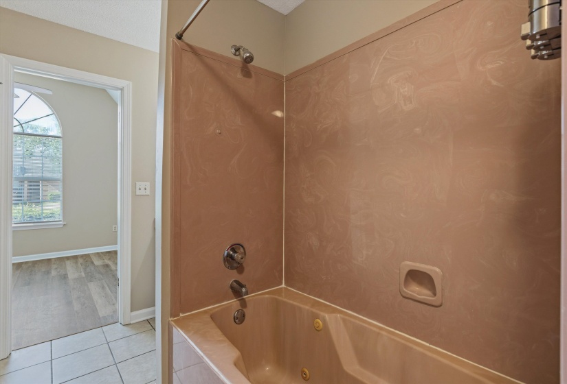 Soaking tub with a tan surround and integrated shower, featuring a chrome shower head and faucet