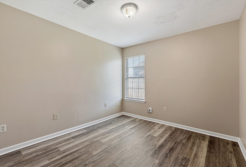 Room featuring wood-finish flooring, neutral wall paint, white baseboards, and a window with blinds