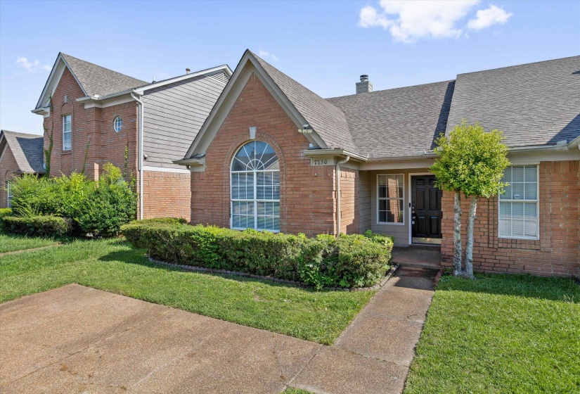 Brick exterior with a prominent arched window, dark shingle roof, and established front landscaping