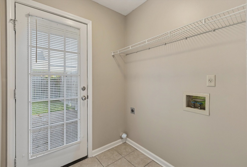 Utility room featuring a glass-paneled exterior door with internal blinds, ceramic tile flooring, a built-in wire shelving unit, and dedicated appliance hookups