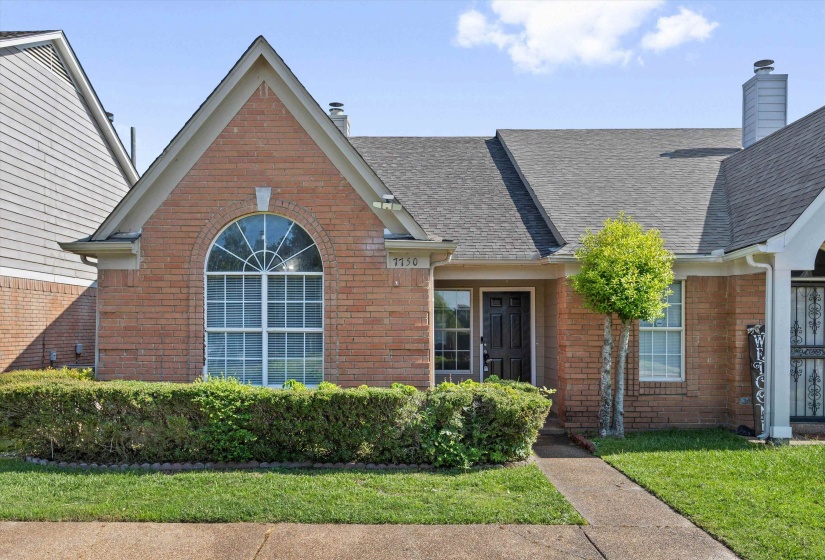 Brick facade home featuring an arched window, dark paneled entry door, and a neatly manicured lawn