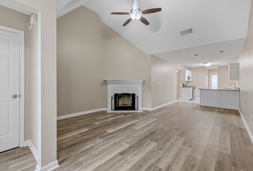 Spacious living area featuring vaulted ceilings, a central fireplace with a classic mantel, wood-finish flooring, and an integrated ceiling fan