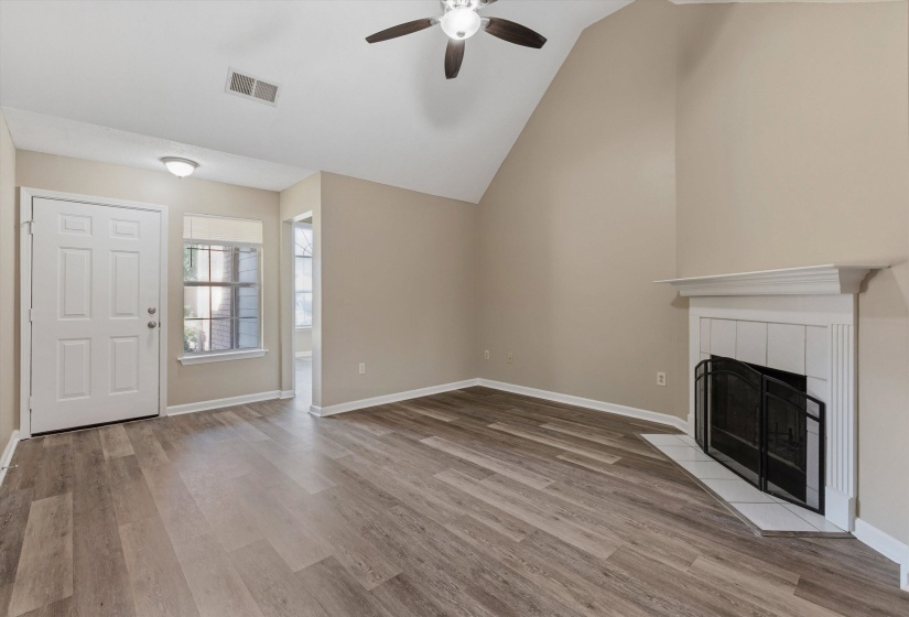 Living room featuring vaulted ceilings, a ceiling fan, a fireplace with a white mantel and tile surround, and wood-finish flooring