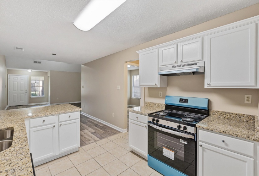 Kitchen featuring light-toned cabinetry, light granite countertops, and a full-size range with an overhead vent